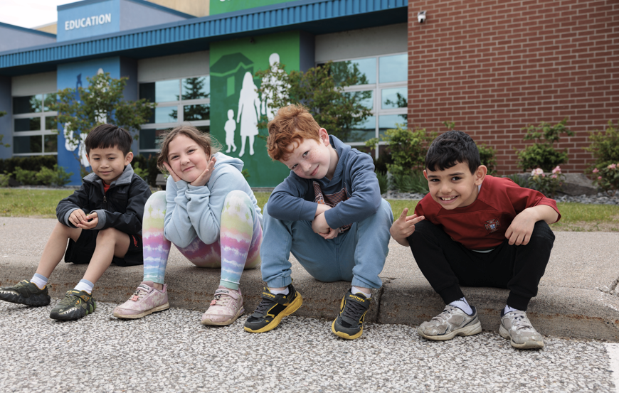 Children sitting in front of building smiling